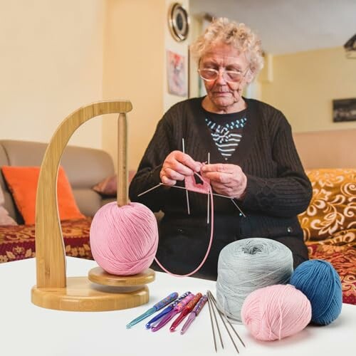 Elderly woman knitting with pink yarn and crochet tools on table.