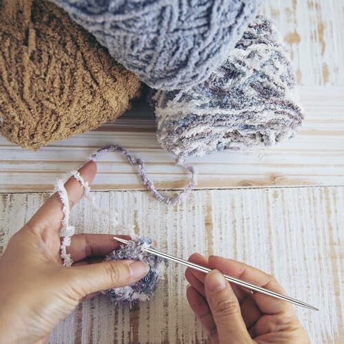 Hands knitting with yarn on a wooden table.