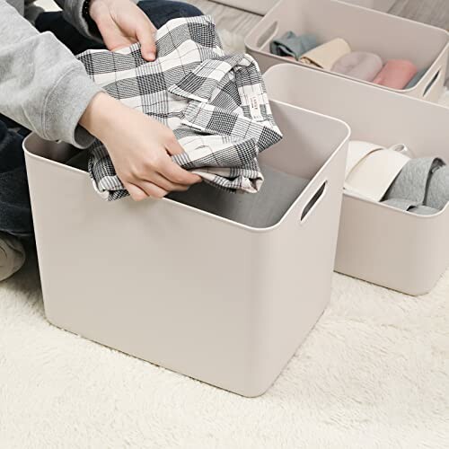 Person organizing clothes into a storage box on a carpeted floor.